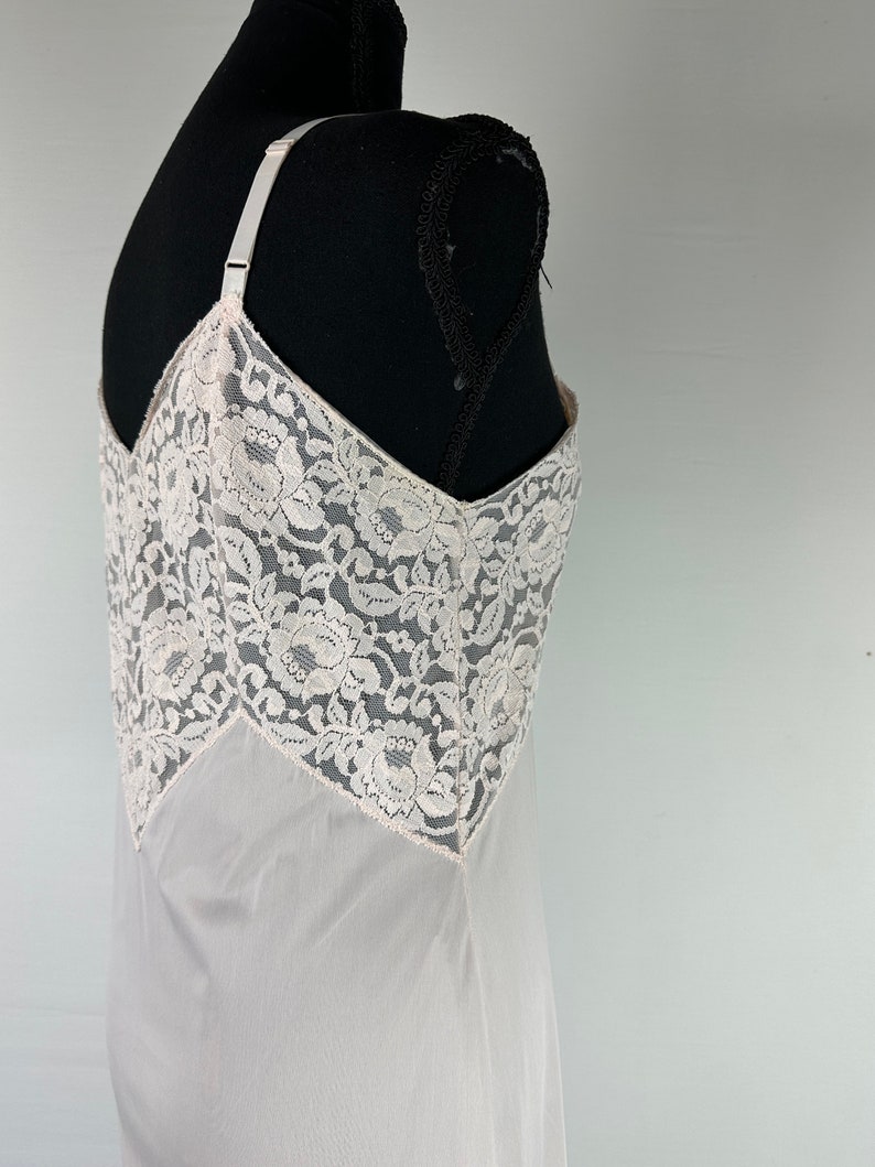 Op de afbeelding: Een witte slip van kant met een delicaat bloemenpatroon. De slip is gemaakt van een transparante stof en heeft verstelbare bandjes.
