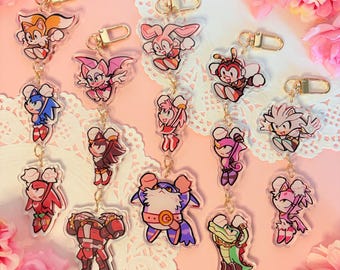 May include: A set of 12 colorful cartoon character keychains featuring characters from the Sonic the Hedgehog video game franchise. The keychains are made of clear acrylic and feature a gold chain.