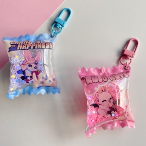 May include: Two pink and blue keychain charms shaped like candy bags with glitter and cartoon characters inside. The blue charm says "Clouds of Happiness" and the pink charm says "Kubo Nuts".