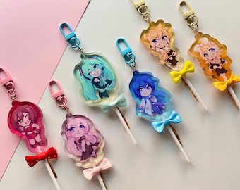 Könnte beinhalten: Sieben bunte Charakter-Schlüsselanhänger mit Lollipop-Stielen und Schleifen. Jeder Schlüsselanhänger zeigt einen anderen Anime-Charakter vor einem transparenten Hintergrund.