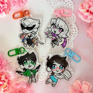 May include: Four clear acrylic keychains featuring cartoon characters with distinct accessories. One has an orange clasp, one pink, one green, and one light blue. The characters include a figure with sunglasses and a sword, a figure holding a drink, a figure with green glasses and two pistols, and a figure with red glasses holding a hat.
