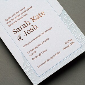May include: A white wedding invitation with a blue and white floral design. The invitation is for Sarah Kate and Josh, and it states the wedding will be held on Saturday, May 6th, 2023 at 3:00 PM at Barnbougle Castle. The RSVP deadline is February 28th.