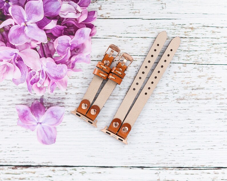 May include: Two brown leather watch bands with gold clasps and a white background. The bands have small holes along the edges.