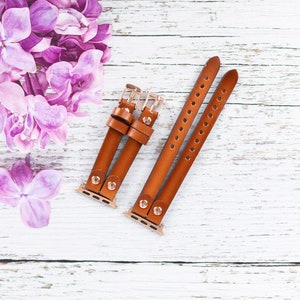 May include: Two brown leather watch bands with gold hardware. The bands are designed for Apple Watches and have a classic look.