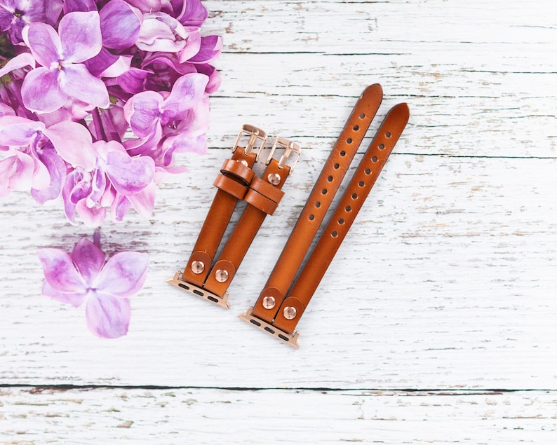 May include: Two brown leather watch bands with gold hardware. The bands are designed for Apple Watches and have a classic look.