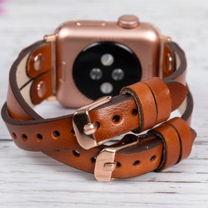 May include: A brown leather double wrap watch band with rose gold hardware. The band is designed to fit Apple Watches.