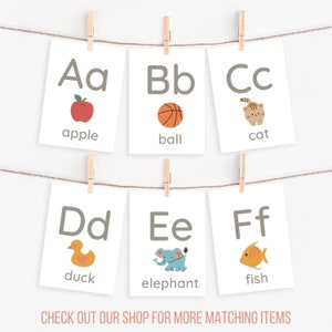 Peut inclure: Six cartes &eacute;ducatives de l'alphabet sont suspendues &agrave; une ficelle par des pinces &agrave; linge. Chaque carte pr&eacute;sente une lettre, un mot et une illustration : pomme, ballon, chat, canard, &eacute;l&eacute;phant et poisson. Le texte "CHECK OUT OUR SHOP FOR MORE MATCHING ITEMS" est en bas.