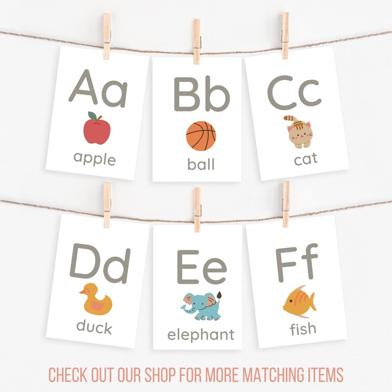 Peut inclure: Six cartes &eacute;ducatives de l'alphabet sont suspendues &agrave; une ficelle par des pinces &agrave; linge. Chaque carte pr&eacute;sente une lettre, un mot et une illustration : pomme, ballon, chat, canard, &eacute;l&eacute;phant et poisson. Le texte "CHECK OUT OUR SHOP FOR MORE MATCHING ITEMS" est en bas.
