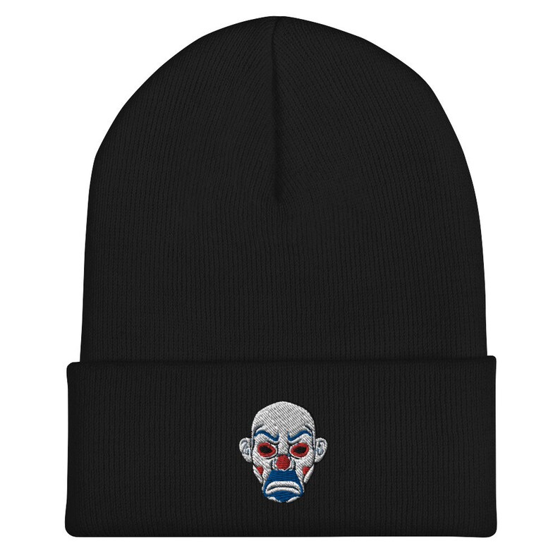K&ouml;nnte beinhalten: Schwarze M&uuml;tze mit einem gestickten Design eines Clowngesichts. Das Clowngesicht hat rote Augen, ein wei&szlig;es Gesicht und einen blau-roten Mund. Die M&uuml;tze ist aus einem weichen, gestrickten Material gefertigt.