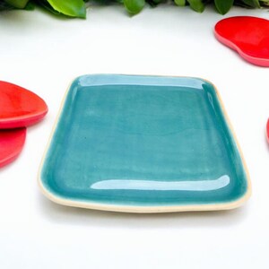 Puede incluir: Un plato rectangular de cerámica de color turquesa con un borde ligeramente elevado. El plato está sobre una superficie blanca.
