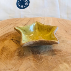 Peut inclure: Un petit plat en céramique en forme d'étoile avec un intérieur émaillé jaune brillant et moucheté, contrastant avec un extérieur en terre cuite brune texturée et non émaillée. Ce bol présente cinq pointes et une forme artisanale organique.