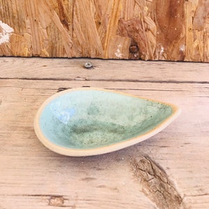 Peut inclure: Un petit plat en céramique bleu clair avec un glaçage moucheté. Le plat est en forme de larme et a un fond légèrement arrondi.