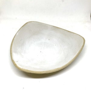 May include: A white ceramic serving dish with a slightly rounded, triangular shape. The dish has a light brown rim and a smooth, white glaze.