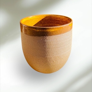 Peut inclure: Une tasse en céramique avec un corps brun clair et un bord jaune. La tasse est émaillée d'une finition mouchetée.