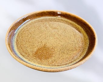 Może przedstawiać: Ręcznie robiony, owalny ceramiczny talerz z nakrapianym, beżowym wnętrzem i ciemniejszą brązową krawędzią. Talerz ma błyszczące wykończenie i subtelne niebiesko-złote szkliwo na krawędzi.