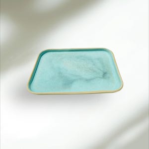 May include: A rectangular ceramic serving tray with a light blue interior and a beige rim. The tray has rounded corners and a smooth, glossy finish. The tray is designed for serving food or displaying decorative items.