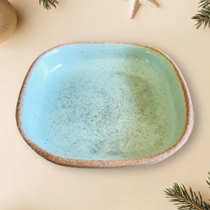 Peut inclure: Un plat de service en céramique bleu clair avec un glaçage moucheté et une forme carrée légèrement arrondie.