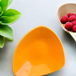 May include: A triangular ceramic dish with a bright yellow glaze. The dish is empty and has a slight curve to the sides.