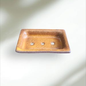 Puede incluir: Un jabonera rectangular de cerámica con un esmalte marrón y tres agujeros de drenaje.