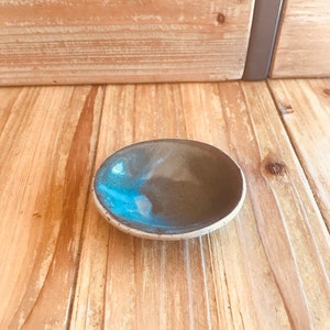Peut inclure: Un petit plat rond en céramique avec un glaçage bleu et gris. Le plat est posé sur une surface en bois.
