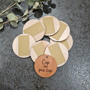 Könnte beinhalten: Ein Satz Holzscheiben mit braunem Hintergrund und einem goldenen Rechteck auf jeder Scheibe. Es gibt eine kleinere Holzscheibe mit dem Text "Cap ou pas cap" auf Französisch.