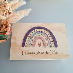 Könnte beinhalten: Holzkiste mit Regenbogen-Design. Der Regenbogen hat Schichten aus lila Glitzer, Türkis, Rosa und Goldglitzer. Auf der Box steht der Text "Les petits trésors de Chloé" eingraviert. In der Mitte des Regenbogens befindet sich ein Herz.