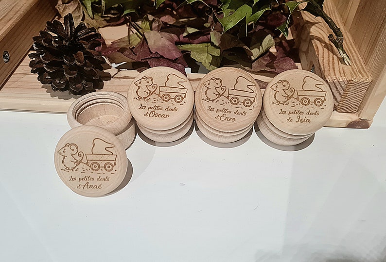 K&ouml;nnte beinhalten: Vier kleine Holzkisten mit Deckel, jede mit einer Maus, die einen Wagen zieht, und dem Text "Les petites dents d'" gefolgt von einem Namen: Oscar, Enzo, Leia und Ana&eacute;.