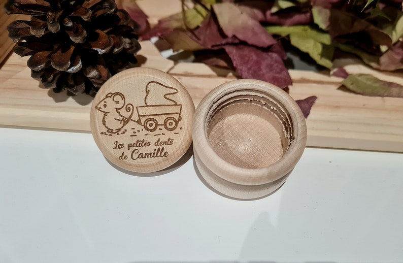 K&ouml;nnte beinhalten: Eine kleine Holzkiste mit Deckel. Der Deckel hat ein Design mit einer Maus, die einen Wagen zieht, mit dem Text "Les petites dents de Camille".