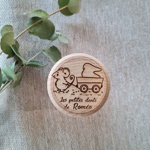 K&ouml;nnte beinhalten: Eine Holzkiste mit einer Maus-Illustration, die einen Wagen mit einem Zahn darin schiebt. Die Kiste ist mit dem Text "Les petites dents de Romeo" graviert.