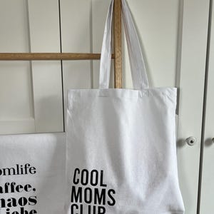 May include: White canvas tote bag with black text that reads "Cool Moms Club".