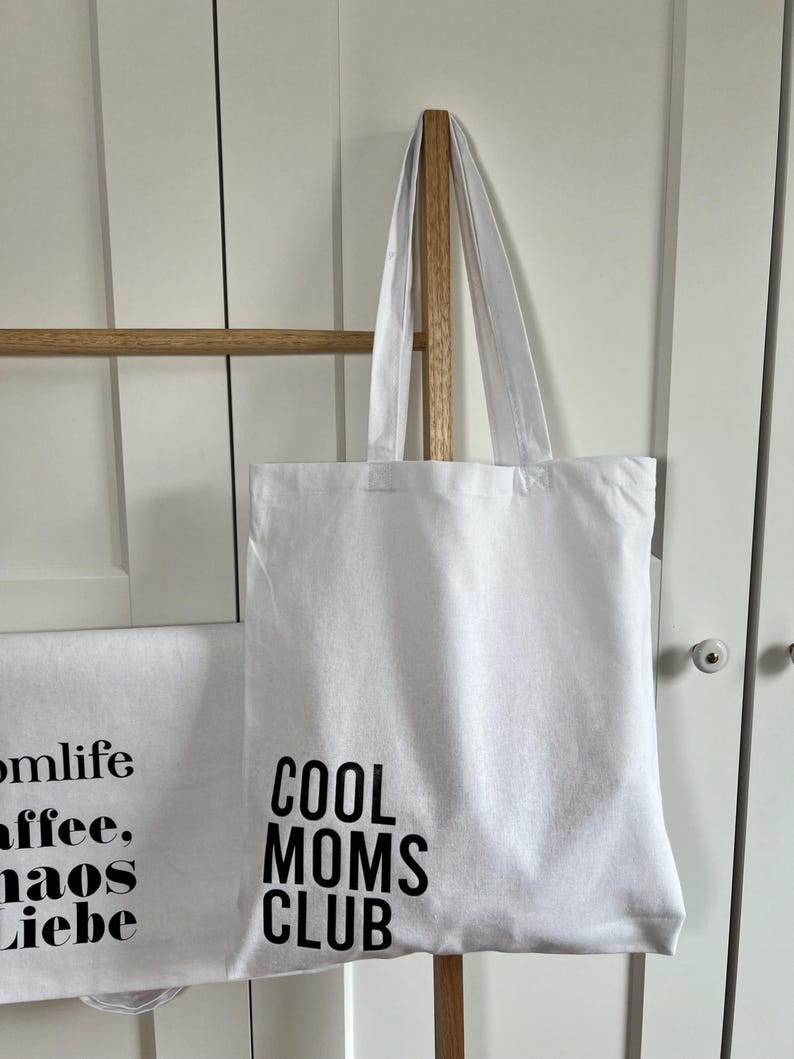 May include: White canvas tote bag with black text that reads "Cool Moms Club".