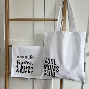 May include: Two white tote bags with black text. One bag says "momlife Kaffee, Chaos & Liebe" and the other says "COOL MOMS CLUB".