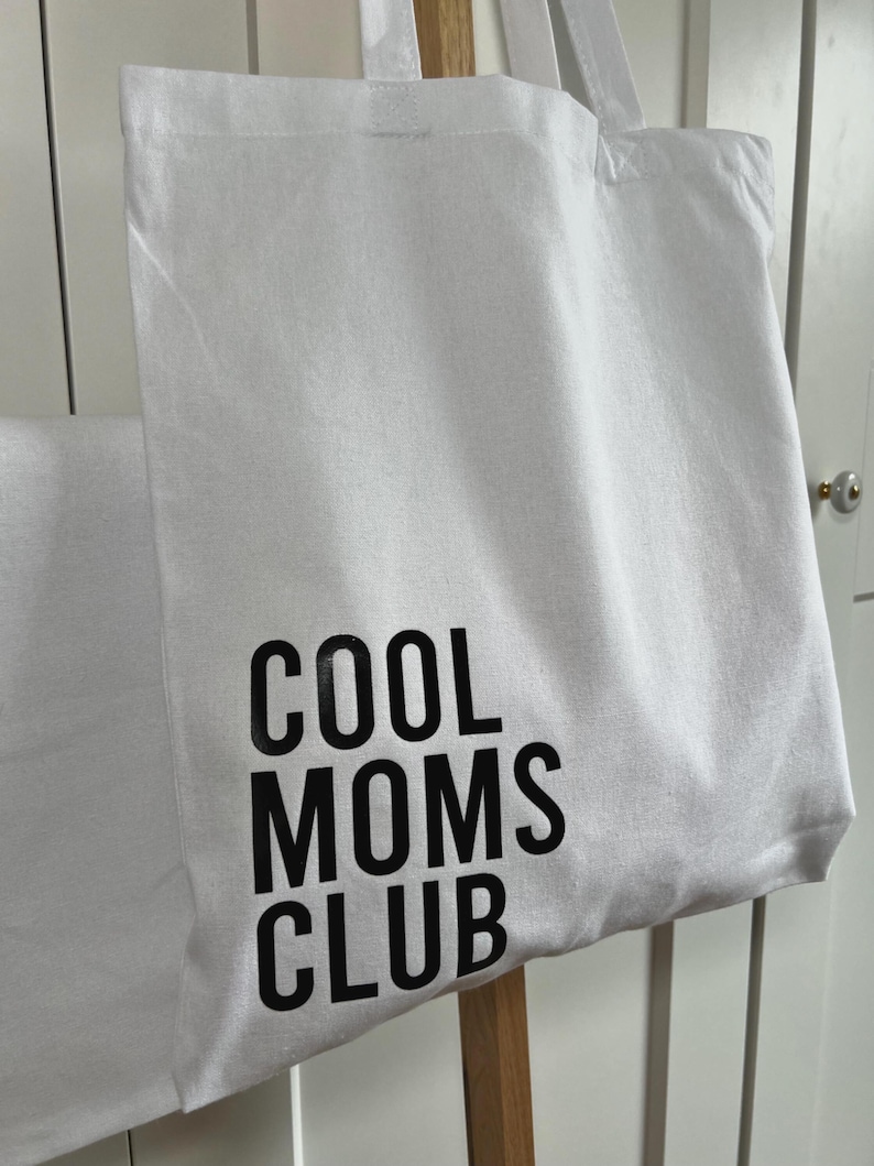 May include: White canvas tote bag with black text that reads "COOL MOMS CLUB".