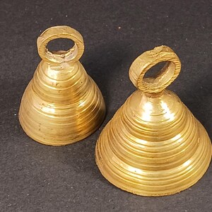 Puede incluir: Dos campanas antiguas de lat&oacute;n con forma c&oacute;nica y un lazo en la parte superior. Las campanas tienen un dise&ntilde;o estriado y un color dorado c&aacute;lido. Probablemente se utilizan para decoraci&oacute;n o como instrumentos musicales.