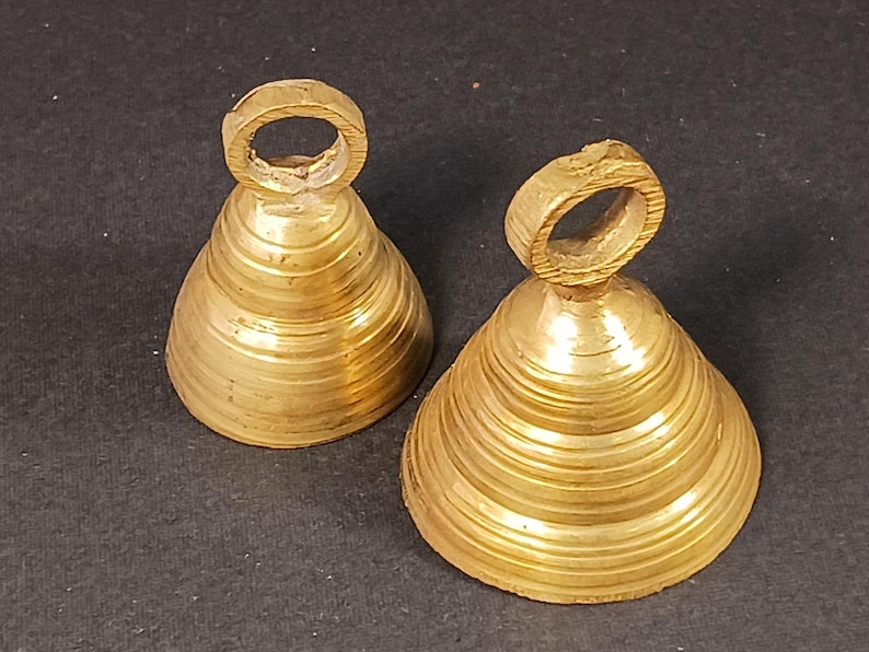 Puede incluir: Dos campanas antiguas de lat&oacute;n con forma c&oacute;nica y un lazo en la parte superior. Las campanas tienen un dise&ntilde;o estriado y un color dorado c&aacute;lido. Probablemente se utilizan para decoraci&oacute;n o como instrumentos musicales.