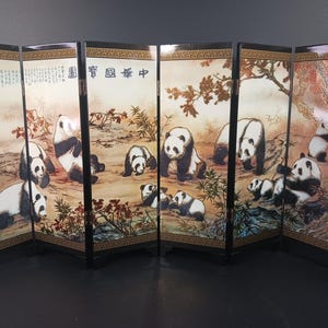 May include: A six-panel folding screen featuring a painted scene of pandas in a natural setting. The artwork depicts several black and white pandas in various poses, surrounded by foliage and trees. The screen has a black frame with gold accents.