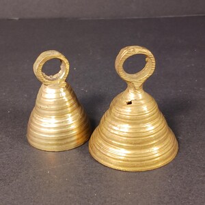 Puede incluir: Dos campanas antiguas de lat&oacute;n con forma c&oacute;nica y un lazo en la parte superior. Las campanas tienen estr&iacute;as horizontales y un color dorado c&aacute;lido. Probablemente se utilizan para decoraci&oacute;n o como instrumentos musicales.