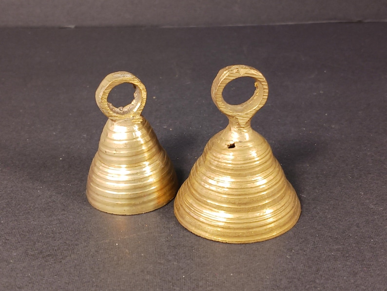 Puede incluir: Dos campanas antiguas de lat&oacute;n con forma c&oacute;nica y un lazo en la parte superior. Las campanas tienen estr&iacute;as horizontales y un color dorado c&aacute;lido. Probablemente se utilizan para decoraci&oacute;n o como instrumentos musicales.