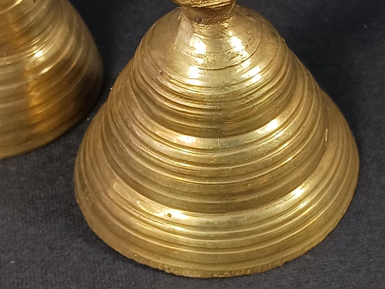 Puede incluir: Primer plano de dos campanas antiguas de lat&oacute;n. Las campanas tienen forma c&oacute;nica con estr&iacute;as horizontales. El lat&oacute;n tiene un tono dorado c&aacute;lido y la superficie muestra signos de edad. Las campanas probablemente se utilizan para decoraci&oacute;n o como instrumentos musicales.