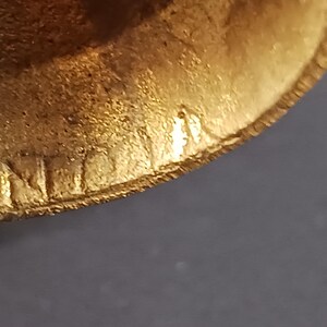 Puede incluir: Primer plano de un objeto dorado con una superficie texturizada. El borde del objeto tiene grabada la palabra "INT". El objeto est&aacute; sobre un fondo oscuro.