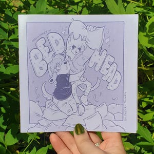 May include: A square print featuring a purple-toned line art illustration of two anthropomorphic animal characters engaged in a pillow fight. The text "MAX + MAZY IN BED HEAD" is written in large bubble letters, with "BY PRESLEY TAYLEN" at the bottom right.