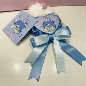 May include: A blue and white heart-shaped pin with a cartoon penguin wearing a hat and holding an Easter egg. The pin is attached to a blue ribbon bow. The text "Tuxedo Sam" is on the pin and the tag.