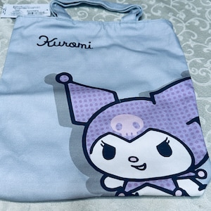 May include: A light blue tote bag with a purple and white cartoon character on it. The character has a skull on its head and the text "Kuromi" is printed on the bag.