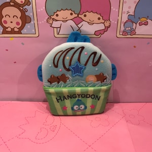 May include: A green and blue plush toy shaped like a fish with the text "HANGYODON" on the front. The toy has a chocolate swirl and a star on top.