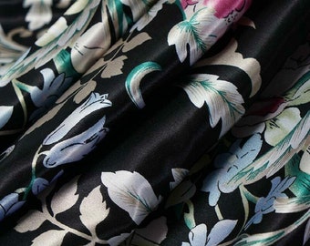 May include: Black satin fabric with a floral print in shades of green, white, and pink. The fabric has a smooth, silky texture.