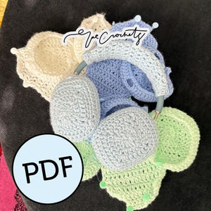 Op de afbeelding: Een verzameling handgemaakte gehaakte hoofdtelefoonhoezen in verschillende pastelkleuren, waaronder lichtblauw, groen en crème. De hoofdtelefoons zijn versierd met decoratieve knopen en de tekst "The Crochetz". Een PDF-afbeelding is ook zichtbaar.