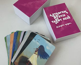 以下が含まれることがあります： ピンクの箱に「Astrofem Mystic Tarot Deck by Rachel Mcbride」という文字が書かれています。カラフルなイラストが描かれたタロットカードの束で、女性がフルートを演奏し、その上に鳥が飛んでいます。カードには「The Fool」と書かれています。