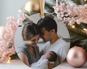 May include: A round glass ornament featuring a photo of a family of three. A couple is holding their newborn baby, with the parents looking at each other lovingly. The ornament is perfect for displaying on a Christmas tree or as a special keepsake.