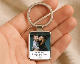 May include: Silver rectangular keyring featuring a photograph of a man and child. The photo includes the text "Drive Safe I Need You Here With Me - Aiden". The keyring has a silver ring.