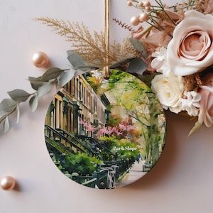 May include: A watercolor painting of a street scene in Park Slope, Brooklyn, New York. The painting features brownstone buildings with steps leading up to the front doors. There are trees lining the street, and the trees are in bloom with pink flowers. The painting is in a circular shape and has a white background.
